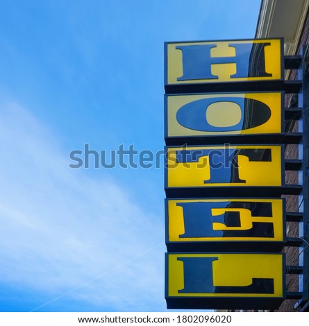 Neon hotel sign on the building corner against blue sky.  Empty copy space for inscription. modern yellow sign. Vertical hotel sign. Amsterdam, Netherlands 