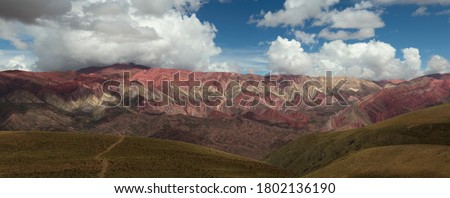 Andes mountain range. Panoramic view of a footpath in the golden valley leading to the colorful Hornocal mountain under a dramatic cloudy sky in Humahuaca, Jujuy, Argentina. Beautiful rock texture. 