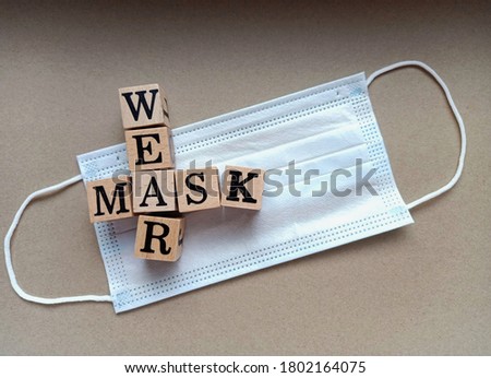 Top view photo of wooden block with crossword WARE MASK placed on a disposable face mask isolated on a brown paper sheet background texture.
