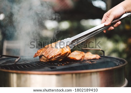 Man hand grilling barbecue with smoked pork at backyard on day. Family dinner outdoor style bbq activity. Royalty-Free Stock Photo #1802189410
