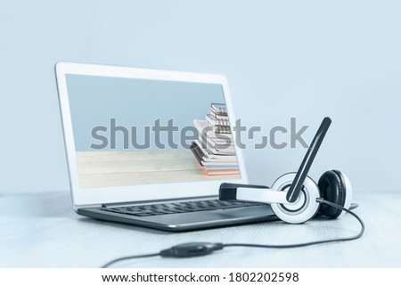 Laptop with pile of notepads on the screen and headphones on white desk blue background. Distant learning or working from home, online courses or school webinar concept.