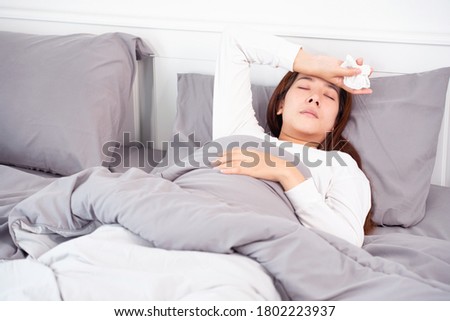 Sick Asian woman with cold sleeping on bed at home with high fever suffering from insomnia 