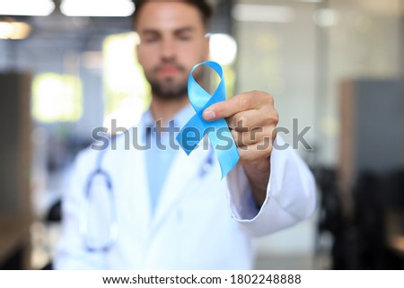 Doctor hand with blue prostate cancer awareness ribbon. Medicine oncology closeup sky symbol.