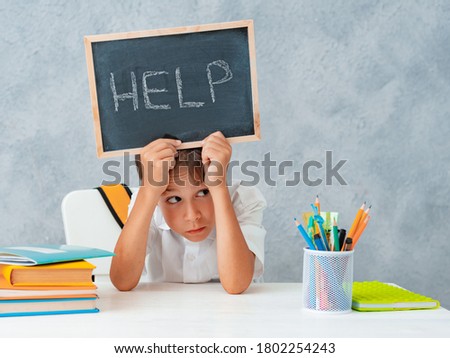 Sad tired frustrated schoolboy boy at the table and holding paper with word Help. Learning difficulties, education concept.
