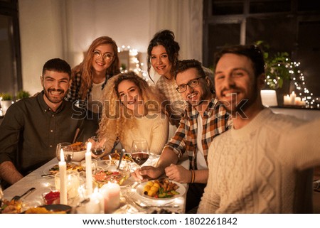 holidays, celebration and people concept - happy friends taking selfie at home christmas dinner party