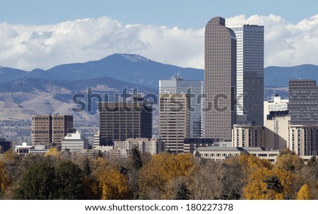 Distinctive Denver, Colorado skyscrapers, with the Rocky Mountains in the background and autumn trees in the foreground.