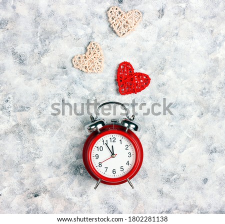 Classical red alarm clock with hearts on gray canvas background. Square top view flat lay image.