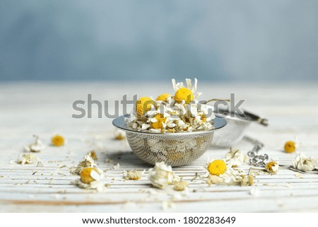 Dry chamomile flowers in infuser on white wooden table, closeup