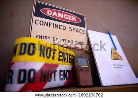 Confined space warning sign permit entry by permit only and red barricade danger tape, yellow caution tape gas test leak atmosphere with defocused confined space permit book template, pen  background 