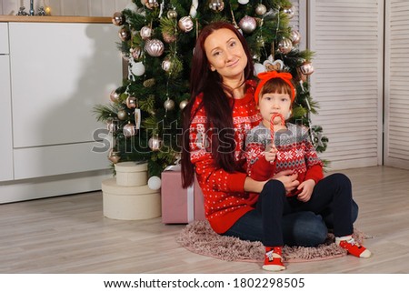 Mom and daughter in red sweaters are sitting by the Christmas tree.