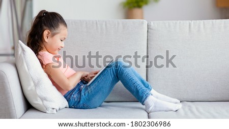 Japanese Kid Girl Using Digital Tablet Computer Watching Cartoons Sitting On Sofa At Home. Child And Gadget. Panorama