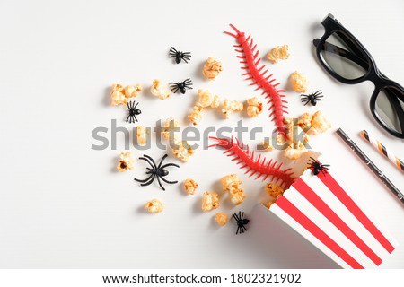 Halloween party background. Flat lay composition with popcorn, halloween decorations, 3d glasses on white table. Watching halloween horror movie at night concept.