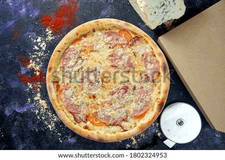 Oven baked italian pizza with melted cheese, ham and tomatoes on a dark background