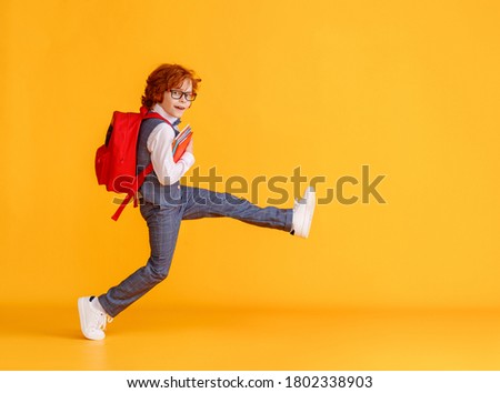 Side view of delighted schoolboy smiling and carrying textbooks while walking to school against yellow backdrop
 Royalty-Free Stock Photo #1802338903