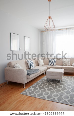 Cozy Scandinavian Living Room. White Chair with cushons and minimalistic decorations. Nordic Minimalism. Apartment furnished in beige and gray neutral colors. 