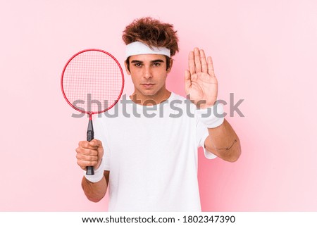 Young man playing badminton isolated standing with outstretched hand showing stop sign, preventing you.