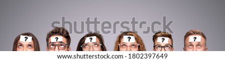 Group of puzzled young people with paper stickers with question mark on foreheads looking up while playing Who Am I game on gray background Royalty-Free Stock Photo #1802397649