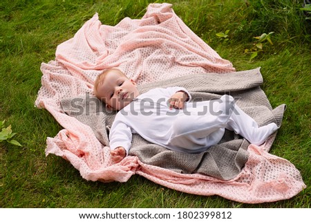  baby in white clothes lies on  knitted blanket, view from above, healthy outdoor recreation