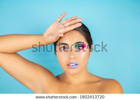 Beauty portrait of female model with vivid makeup on one half of the face and clean face on the other part on blue background and blue lips.