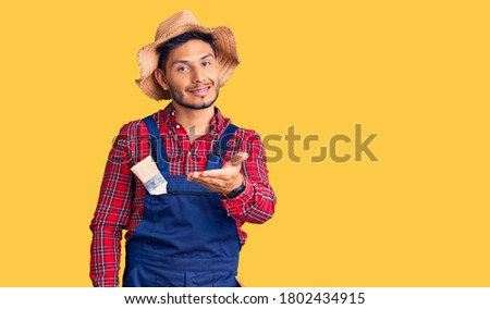 Handsome latin american young man weaing handyman uniform smiling cheerful offering palm hand giving assistance and acceptance. 