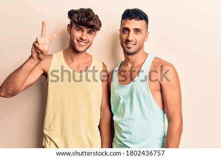Young gay couple wearing casual clothes showing and pointing up with fingers number two while smiling confident and happy. 