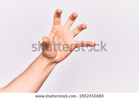 Close up of hand of young caucasian man over isolated background grasping aggressive and scary with fingers, violence and frustration  Royalty-Free Stock Photo #1802450680