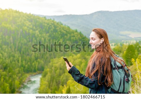 Happy woman holds smartphone at mountains and using travel app or map during her hike