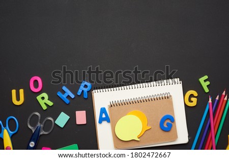 colorful wooden pencils, notebook on a blank black chalk board, school stationery, copy space, back to school 