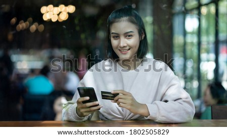 Portrait of an Asian teenage woman chill out and make payment through credit card and smart phone in the cafe. Stock photo.