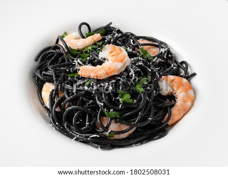 Black Italian seafood pasta with shrimps and greens on white restaurant plate. Black homemade spaghetti, noodles with cuttlefish ink, cooked sea food macaroni closeup