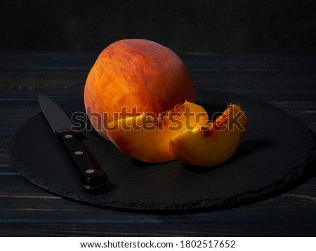 A whole juicy peach, two pieces of peach with black knife on the dark stone plate and dark wooden background. Close up.  Royalty-Free Stock Photo #1802517652