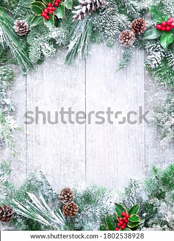 Christmas and New Year background with fir branches, holly and snowfall on wooden white board