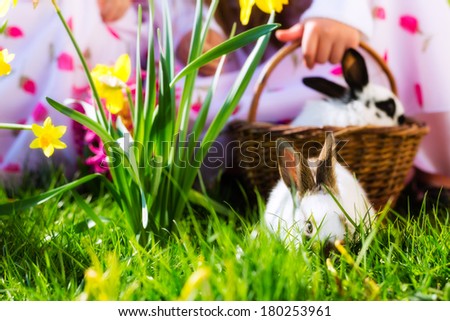 Living Easter bunny in a basket on a meadow in spring, children in the background