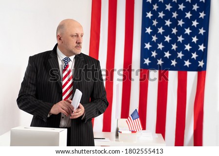 USA election. Voter has a bill over the vote. USA flags in background. Democracy concept. Election in United States of America. Man wants to put a billboard in urn. US presidential elections. Voter US