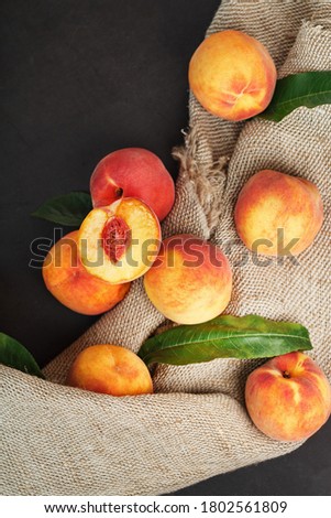 Peaches on a black background with burlap fabric and green leaves. Sweet and juicy peach slices with a stone