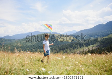 little boy holds string of kite flying in blue sky with clouds in summer with copyspace