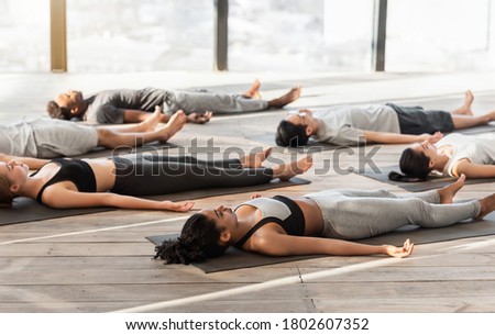 Group of sporty people relaxing during yoga lesson, lying on floor in Corpse pose, doing Shavasana, free space Royalty-Free Stock Photo #1802607352
