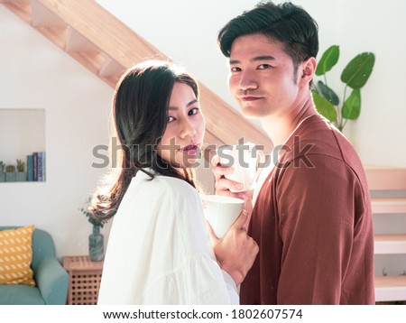 Young asian man and woman at home with cup of coffee in hands.