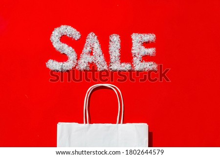 Seasonal sale, Black Friday, new year discounts and shopping concept. Sale sign and a paper shopping bag on a red background. Flat lay.