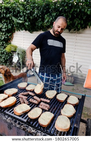Minced meat called cevapi or cevapcici and slices of bread turned with tweezers on a charcoal grill. Barbecue in the back yard garden.

