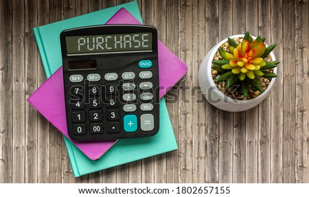 Purchase the text on the calculator, which lies on multi-colored notebooks and with a cactus flower on a wooden table
