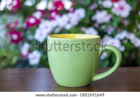 Coffee cup mockup on a garden table. Green color blank mug with handle for hot beverage, blur blooming flowers background. Advertise, branding template