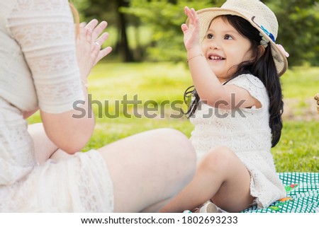 Little Hispanic girl playing with her mother on a picnic in the field surrounded by trees - girl smiling and giving the 5 to her mother in the middle of nature