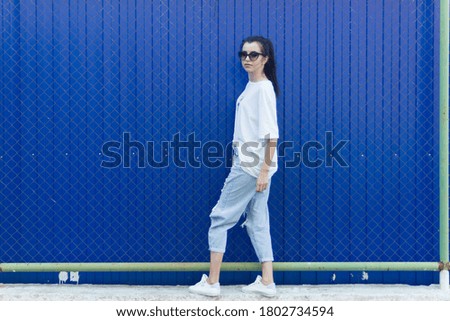 Girl in a white T-shirt and black glasses on the background of a blue metal wall
