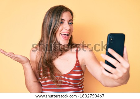 Beautiful young caucasian woman taking a selfie photo with smartphone celebrating achievement with happy smile and winner expression with raised hand 
