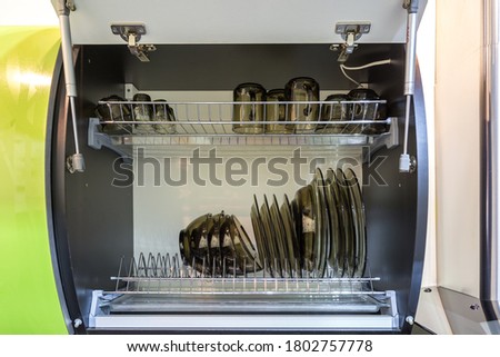 set of plates, cups, knives, forks and wine glasses on the shelf in the kitchen cabinet