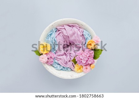 background for a photo shoot of a newborn baby in a white wooden bowl with a pink and blue cloth and with pink hydrangeas, yellow roses on a blue background