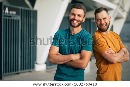 Two happy friends or brothers in colorful t-shirts are standing back to back with crossed arms outdoors Royalty-Free Stock Photo #1802760418