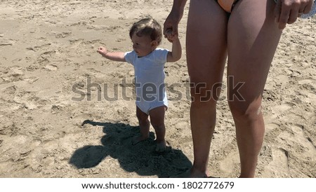 
Toddler baby learning to walk with help of mother holding hands at beach
