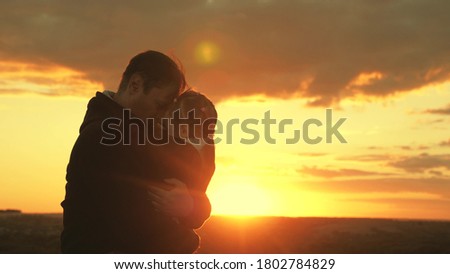 Happy child and father are playing in field in sun. dad hugs and covers his little daughter with jacket on cool evening in park at sunset. healthy baby kisses daddy. happy family and childhood concept